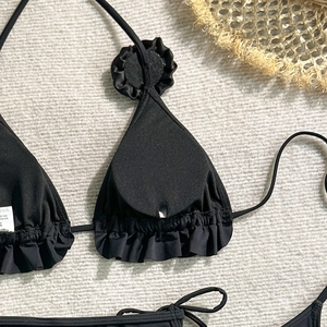 Detailed close-up of a black bikini top with ruffled edges and floral accents on S size