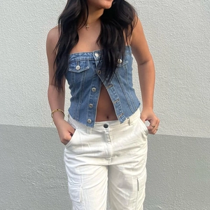 Détail du haut bandeau en denim bleu avec boutons métalliques, poches et coupe ajustée