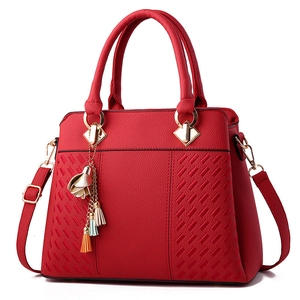 Elegant red leather handbag with lychee texture and floral tassel charm on white background