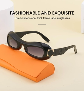 Detail view of oval Y2K sunglasses with black frame and gradient gray lenses on an orange case