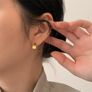 Close-up of minimalist gold rectangular stud earrings worn on a model's ear