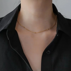 Elegant gold beaded snake chain choker necklace displayed on a model in a black shirt