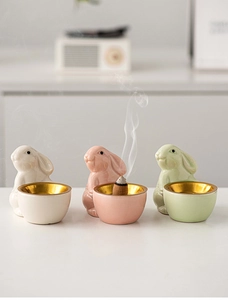 Detailed view of ceramic rabbit incense burners in pink, cream and green with burning cone
