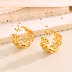 Macro shot of gold wide C-shape hollow woven earrings on a beige textured stone base