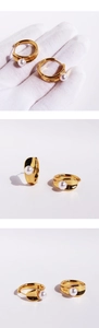 Macro detail of gold hoop earrings featuring polished metal finish and round white pearls