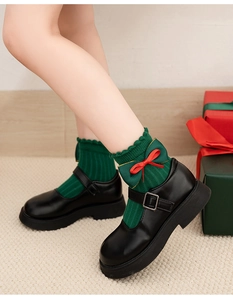 Detail of green Christmas socks with red bows paired with black Mary Jane shoes