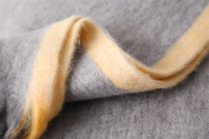 Detailed close-up of soft grey and yellow cashmere-like fabric texture with fringe
