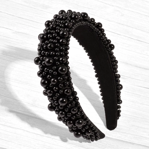 Close-up of wide black padded headband featuring dense glossy pearl embellishments on wood