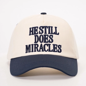 Detail of embroidered HE STILL DOES MIRACLES text on a navy and cream baseball cap