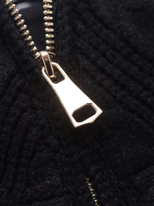 Detailed close-up of a golden metal zipper on a black knitted casual jacket fabric