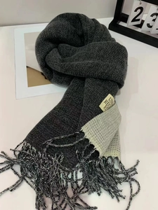 Close-up of thick grey knit scarf with beige block, fringes, and UNI REG ES woven label