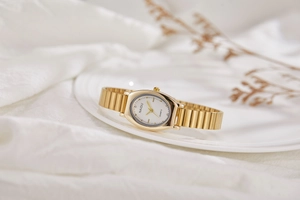 Detail view of oval gold watch with white dial and delicate metallic strap on fabric