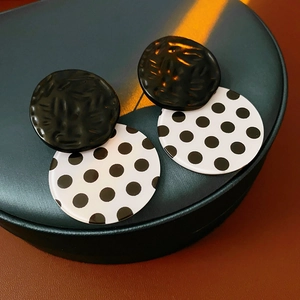 Detail of polka dot acrylic drop earrings displayed on a dark green jewelry box