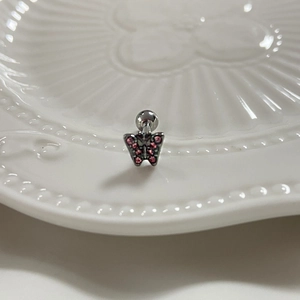 Détail d'un piercing de langue papillon argenté avec strass roses sur plat blanc