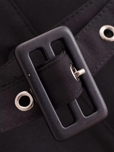 Detailed close-up of a black fabric belt with silver metal grommets and a rectangular buckle