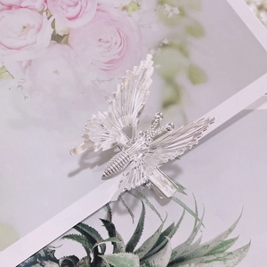 Macro shot of a silver butterfly hair clip with detailed wings on a floral background