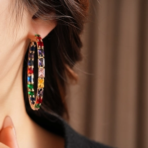 Macro side view of a large gold hoop earring with multicolor baguette zircon stones