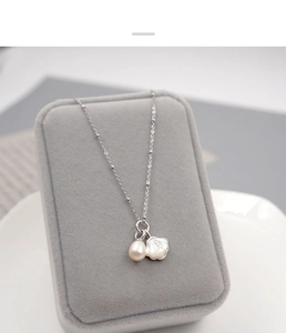 Macro shot of silver necklace featuring freshwater pearl and seashell charms on velvet box