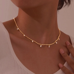 Close-up of a gold ball chain necklace with seven square zircon stones on a model