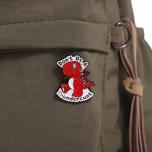 Funny red T-Rex enamel pin with humorous text on olive green canvas bag background