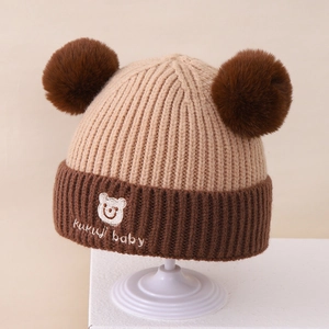 Detailaufnahme der warmen Baby-Strickmütze mit Plüschbommeln und süßer Bärenstickerei