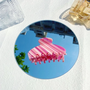 Pince à cheveux Y2K en acétate rayé rose posée sur un miroir reflétant le ciel bleu