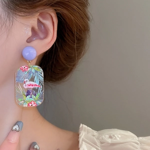 Close-up of long tropical drop earrings with pink flamingo and palm leaf acrylic detail