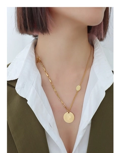 Detail of gold asymmetric necklace with coin pendant worn over white shirt and blazer