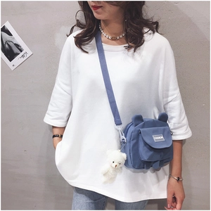 Detailed view of a blue canvas crossbody bag with a cute white plush bear pendant