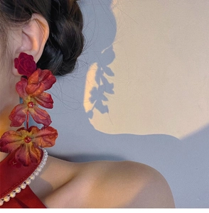 Detailed close-up of long layered red floral tassel earrings worn on ear in soft natural light