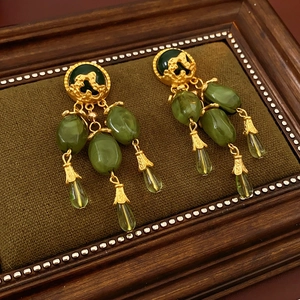 Macro detail of vintage gold earrings with olive green gems on dark velvet padding