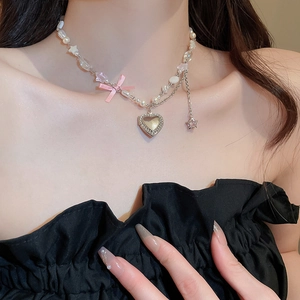 Gros plan d'un collier multicouche avec nœud rose, médaillon cœur et perles sur la clavicule