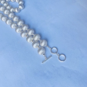 Vue macro d'un collier de perles argentées au fini brossé mat et fermoir à bascule OT