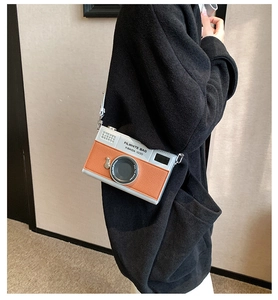 Detail of silver and orange camera-shaped bag with adjustable strap on a black outfit