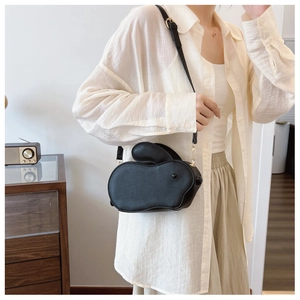 Détail d'un sac bandoulière noir en forme de lapin porté avec une tenue beige chic