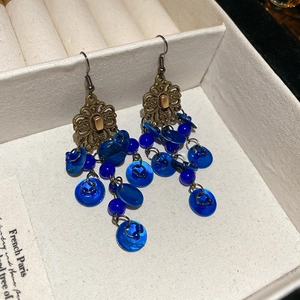 Close-up of vintage bronze earrings with blue sequins and round beads on decorative card