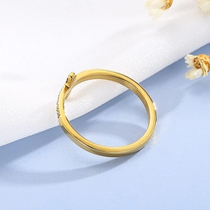 Détail macro d'une bague croix dorée sertie de zircons sur tissu blanc et fond bleu clair