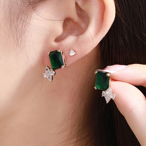 Macro shot of long drop earrings with emerald green gemstones and marquise diamond accents