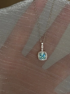 Detail of silver necklace featuring a square light blue gemstone with halo diamonds