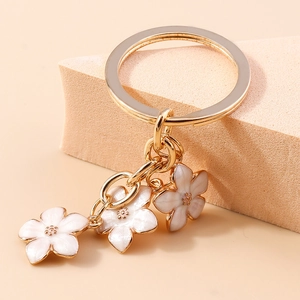 Close-up of golden sakura flower keychain with white enamel petals on warm background