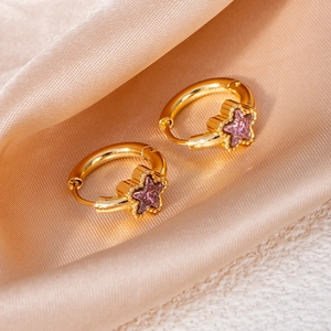 Detail of gold star hoop earrings featuring purple zircon stones on silk background
