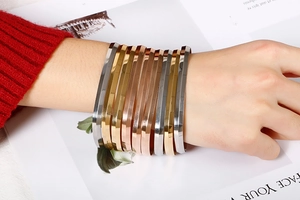 Close-up of stacked gold, silver, and rose gold square bangles with faceted metallic finish