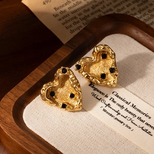 Lava texture heart-shaped gold earrings with black gemstone on a wooden vintage display