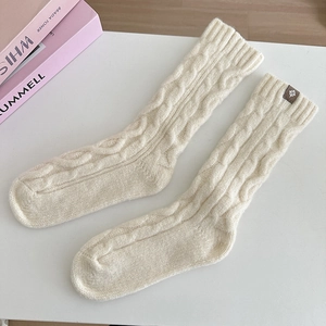 Detail of cream cable knit wool socks featuring a minimalist brown leather logo patch