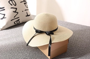 Close-up of the woven straw texture and black ribbon bow on a beige wide-brim sun hat