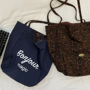 Flat lay view of a large leopard print tote bag next to a navy blue nylon commuter bag