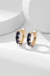 Macro detail of gold huggie earrings with prong-set deep blue cubic zirconia stones