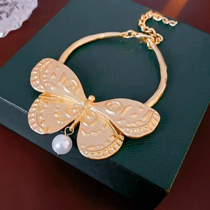Close-up of golden butterfly pendant with textured wings and white pearl drop on jewelry box