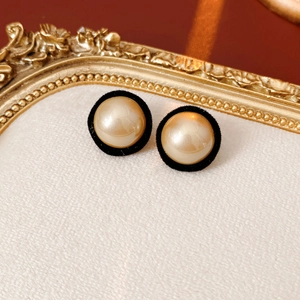 Detail of vintage round champagne pearl earrings with black velvet rim on a beige surface