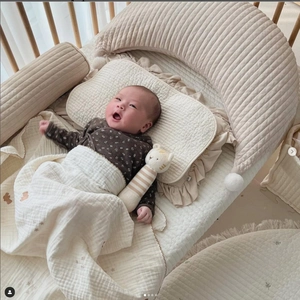 Top view of cream cotton quilted baby bedding set with moon pillow in a cozy crib